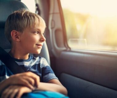 Jongen kijkt tijdens een lange autorit door het zijraam naar buiten