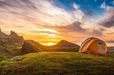 Oranje tent in een berglandschap bij zonsopkomst aan zee